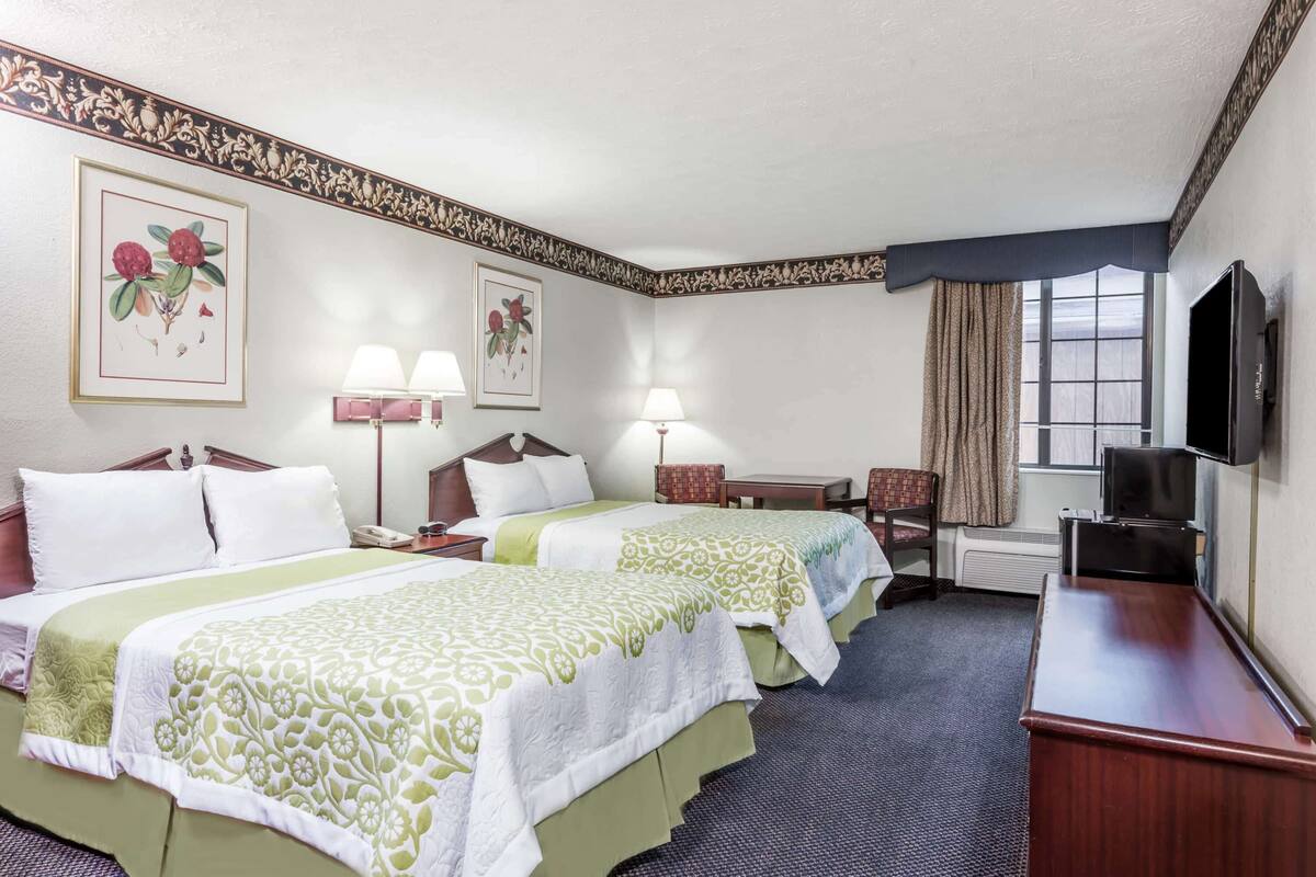 Une chambre d’hôtel avec deux lits, un bureau, une chaise, une télévision et une fenêtre avec des rideaux.