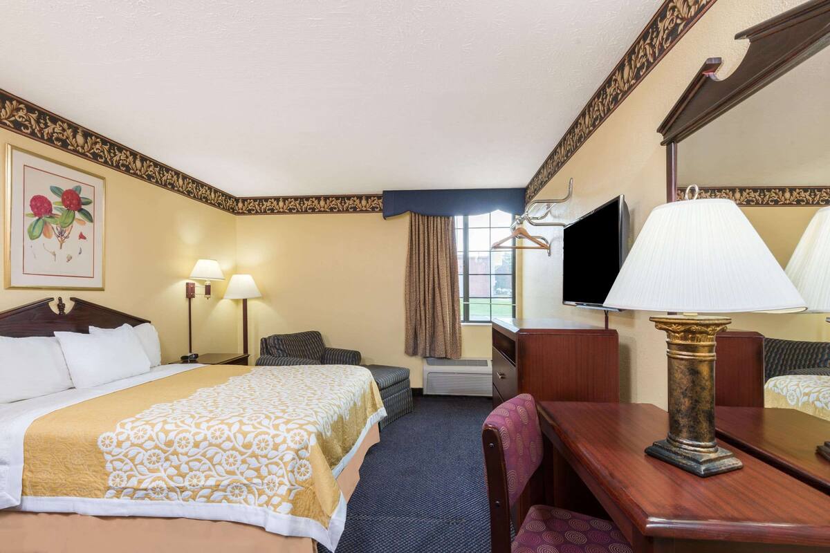 Une chambre d’hôtel avec un grand lit, un bureau, une chaise, une télévision et une fenêtre avec des rideaux.