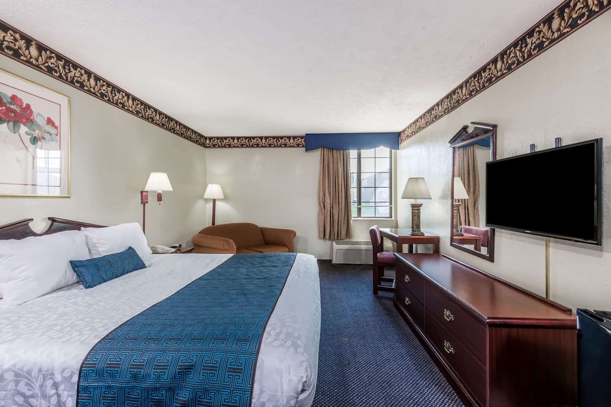 Une chambre d’hôtel avec un grand lit, deux lampes de chevet, une télévision, une commode et une fenêtre avec des rideaux.