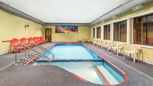 Una piscina interior con sillas rojas y blancas, un mural y vistas al exterior.