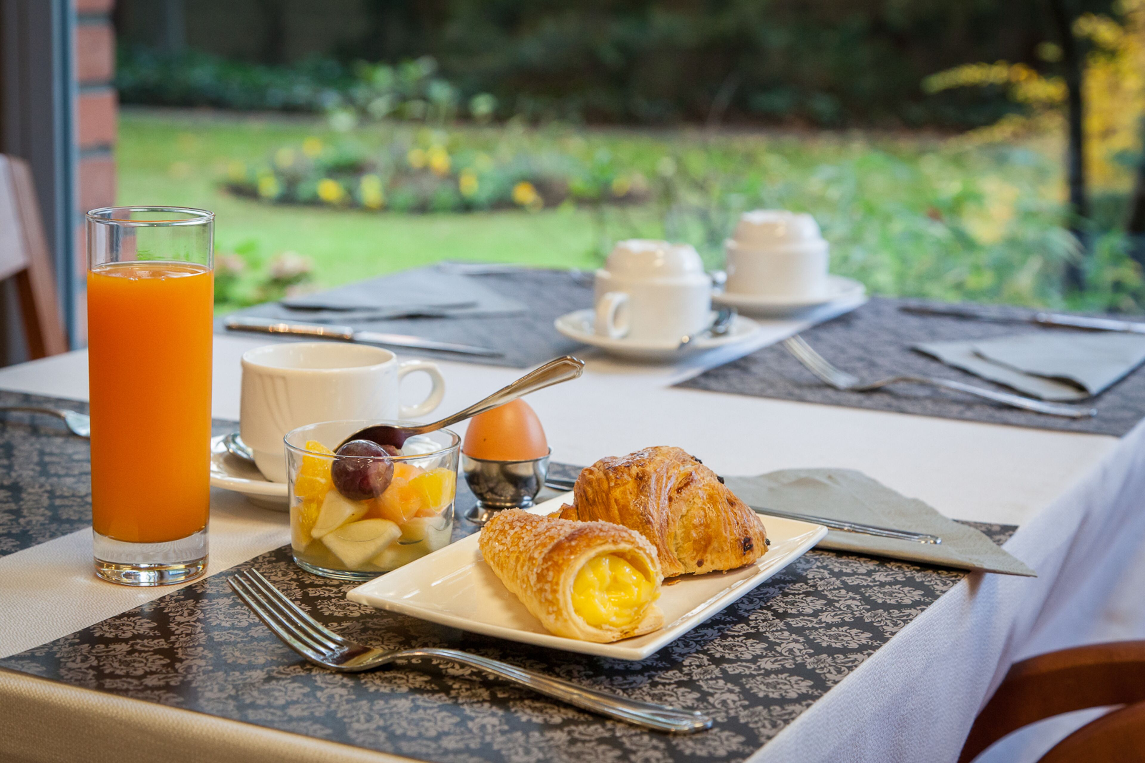 Un desayuno con un croissant, fruta, un vaso de jugo de naranja y una taza de café sobre una mesa.