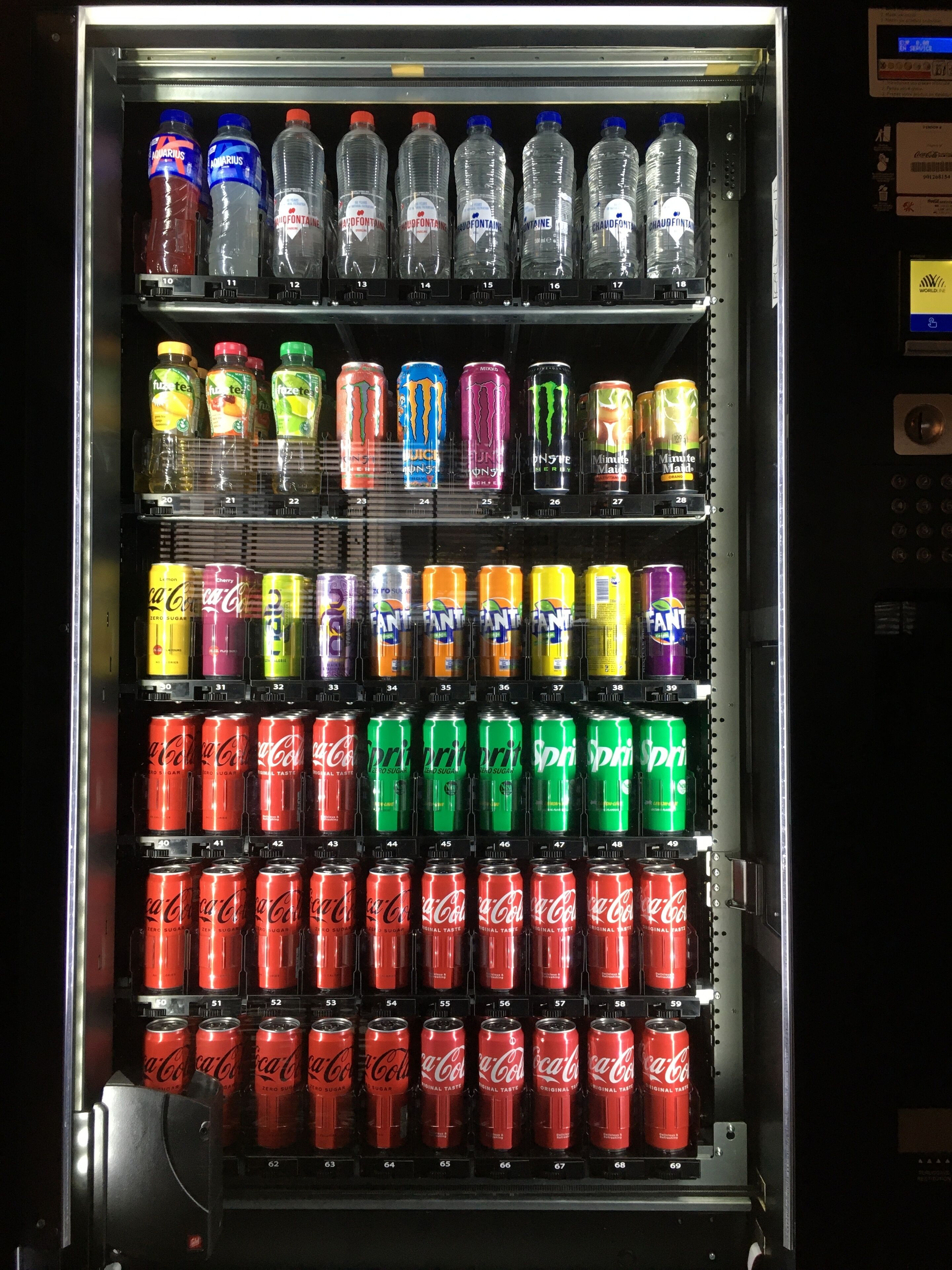 A vending machine stocked with various beverages including water, energy drinks, and sodas.
