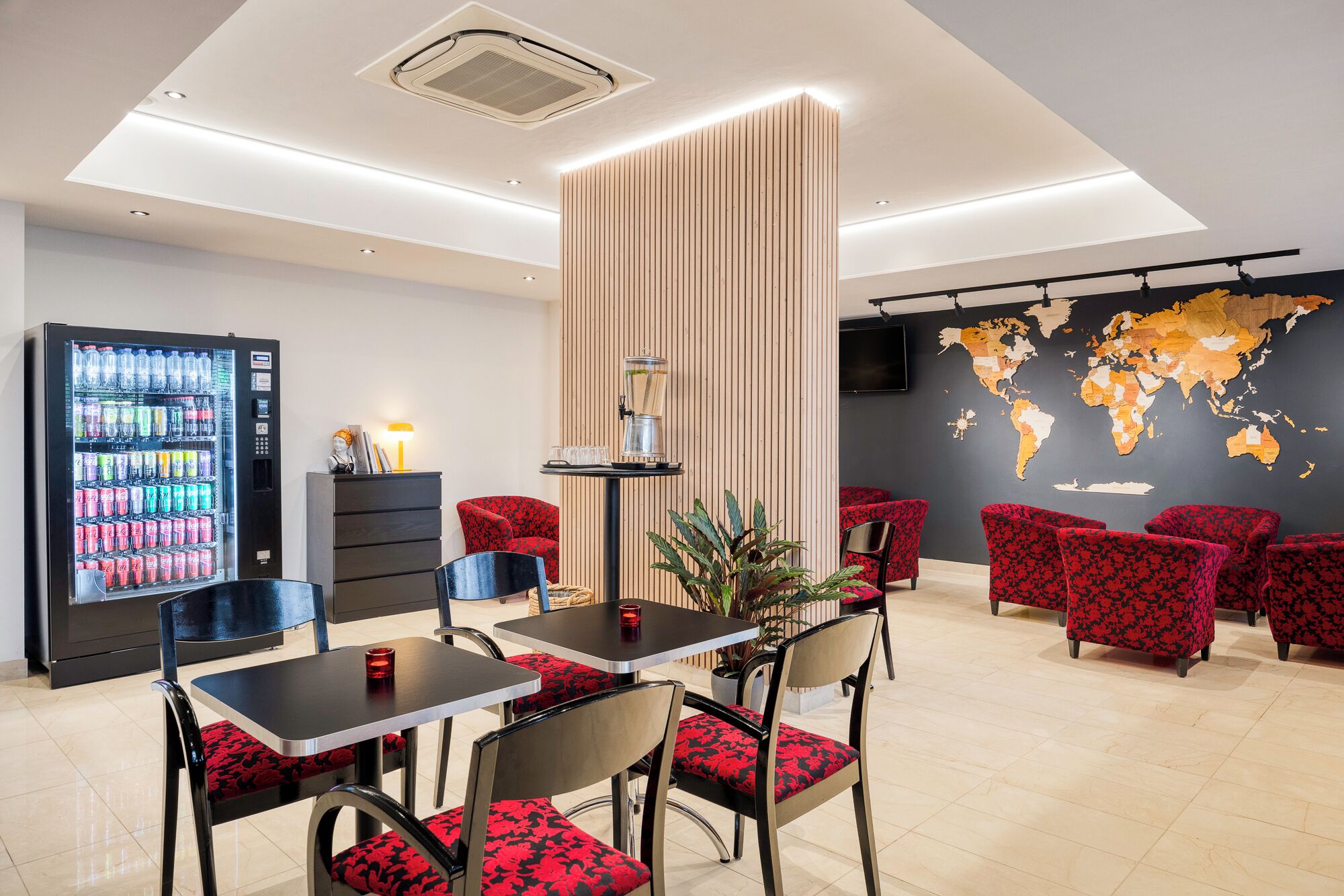 Un moderno vestíbulo de hotel con una máquina expendedora, un mapa mundial en la pared y sillones tapizados de color rojo.