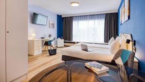 Une chambre d’hôtel avec un lit, un bureau, une chaise et une table sur laquelle se trouve un livre.
