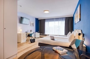 Et hotelværelse med seng, skrivebord, stol og et bord med en bog.