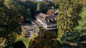 A hotel with a traditional architectural style, featuring a central courtyard with outdoor seating and umbrellas, surrounded by dense forest. - Bilderberg De Bovenste Molen Hotel (Venlo)