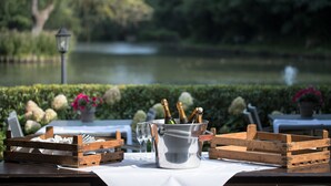 A table set with a metal bucket containing bottles, glasses, and cutlery, with a scenic lake view in the background. - Bilderberg De Bovenste Molen Hotel (Venlo)