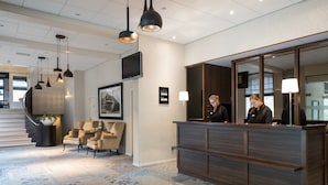 A reception area with a wooden reception desk, a large mirror, and a seating area with chairs. - Bilderberg De Bovenste Molen Hotel (Venlo)