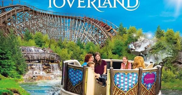 A water ride with a wooden boat, a water wheel, and a roller coaster in the background.
