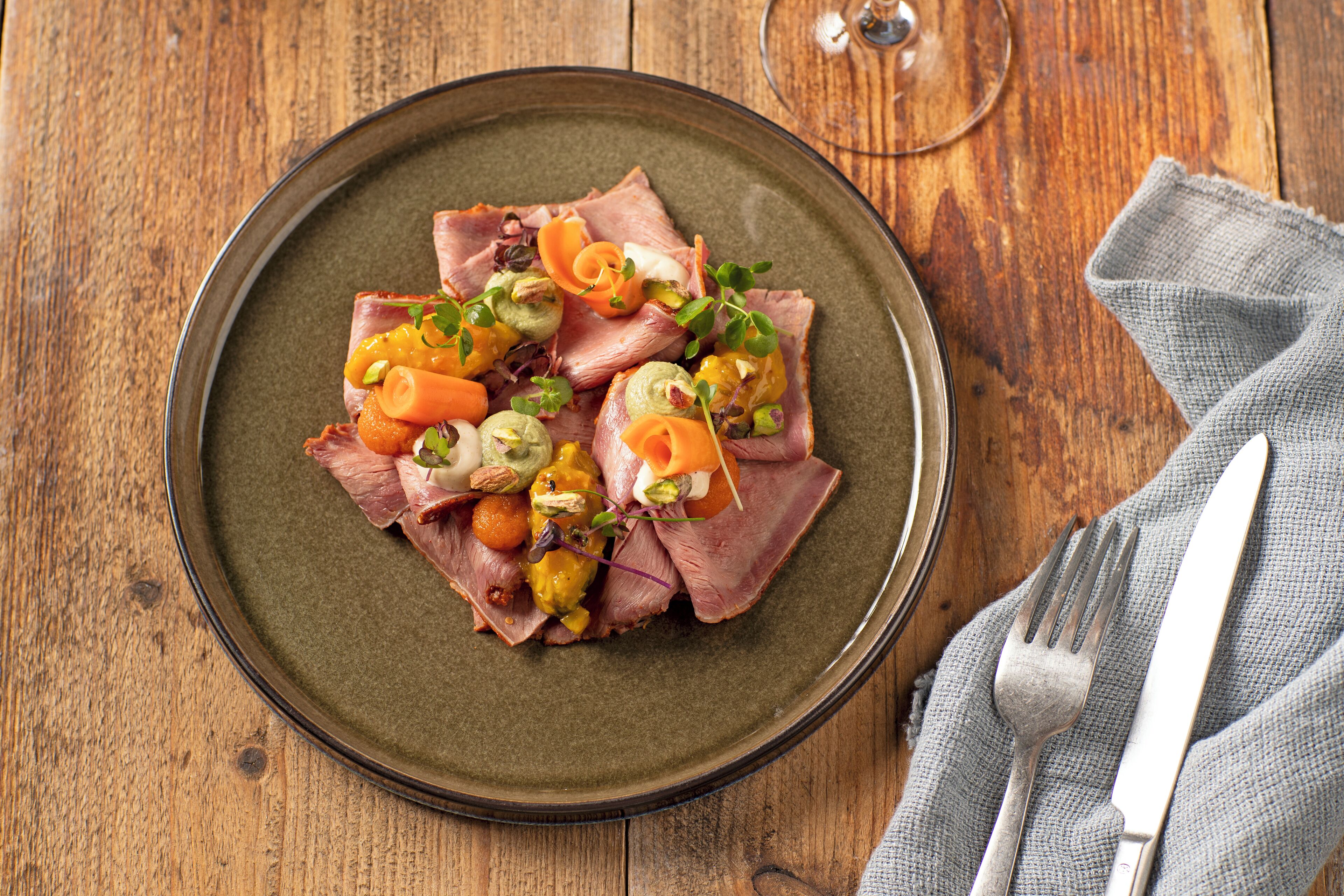 Un plato de carne en rodajas, verduras y nueces sobre un plato de cerámica.
