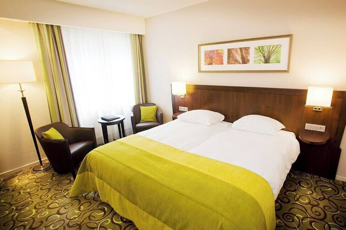 Habitación de hotel con una cama grande, dos mesitas de noche, una silla, un escritorio y una ventana con cortinas.