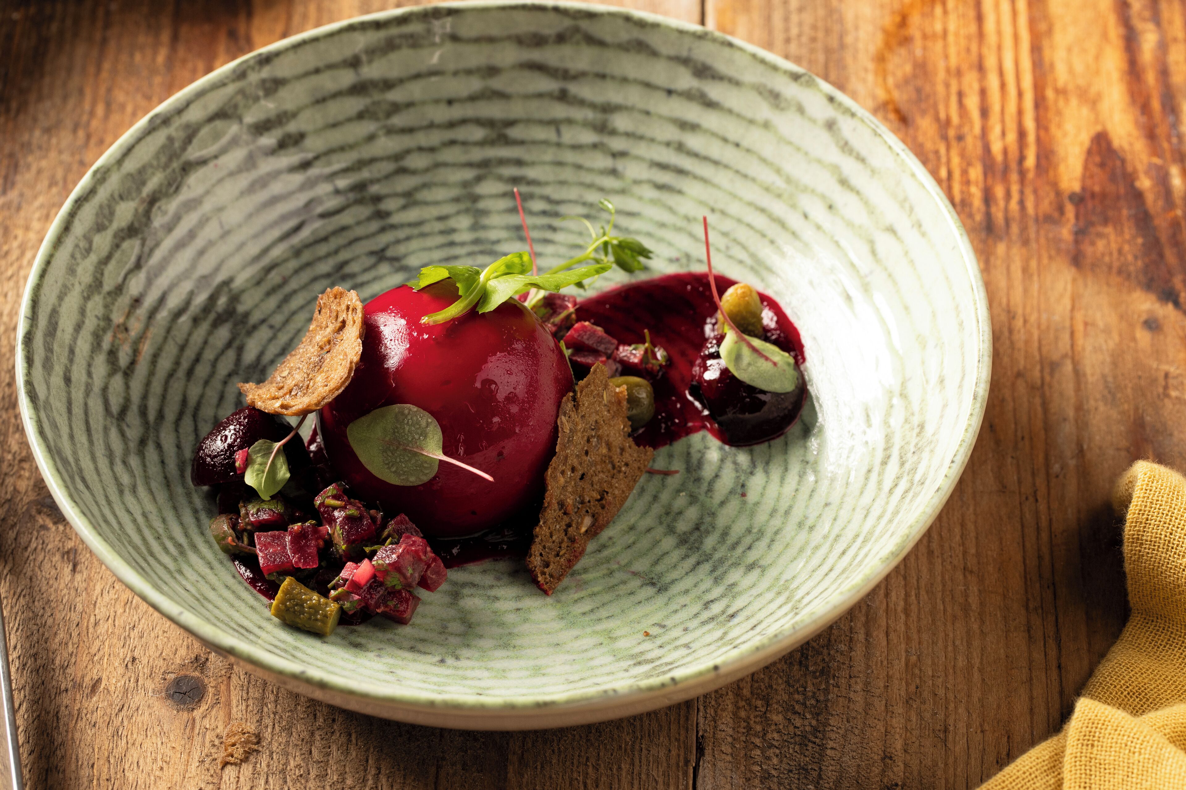A ceramic bowl with a rustic design, containing a beetroot salad with greens and croutons, on a wooden surface.