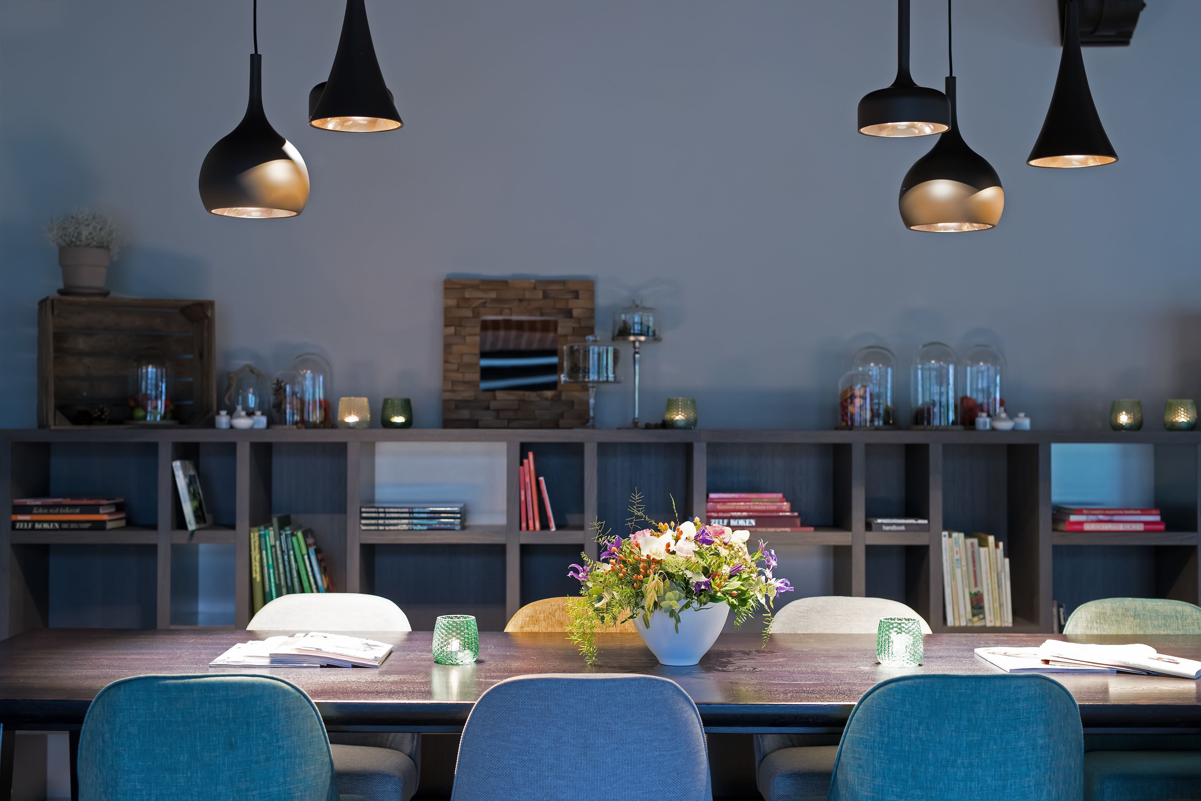 A modern dining area with a wooden table, blue chairs, and black pendant lights.