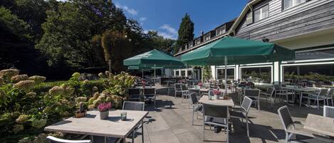 An outdoor patio area with tables and chairs, green umbrellas, and potted plants.