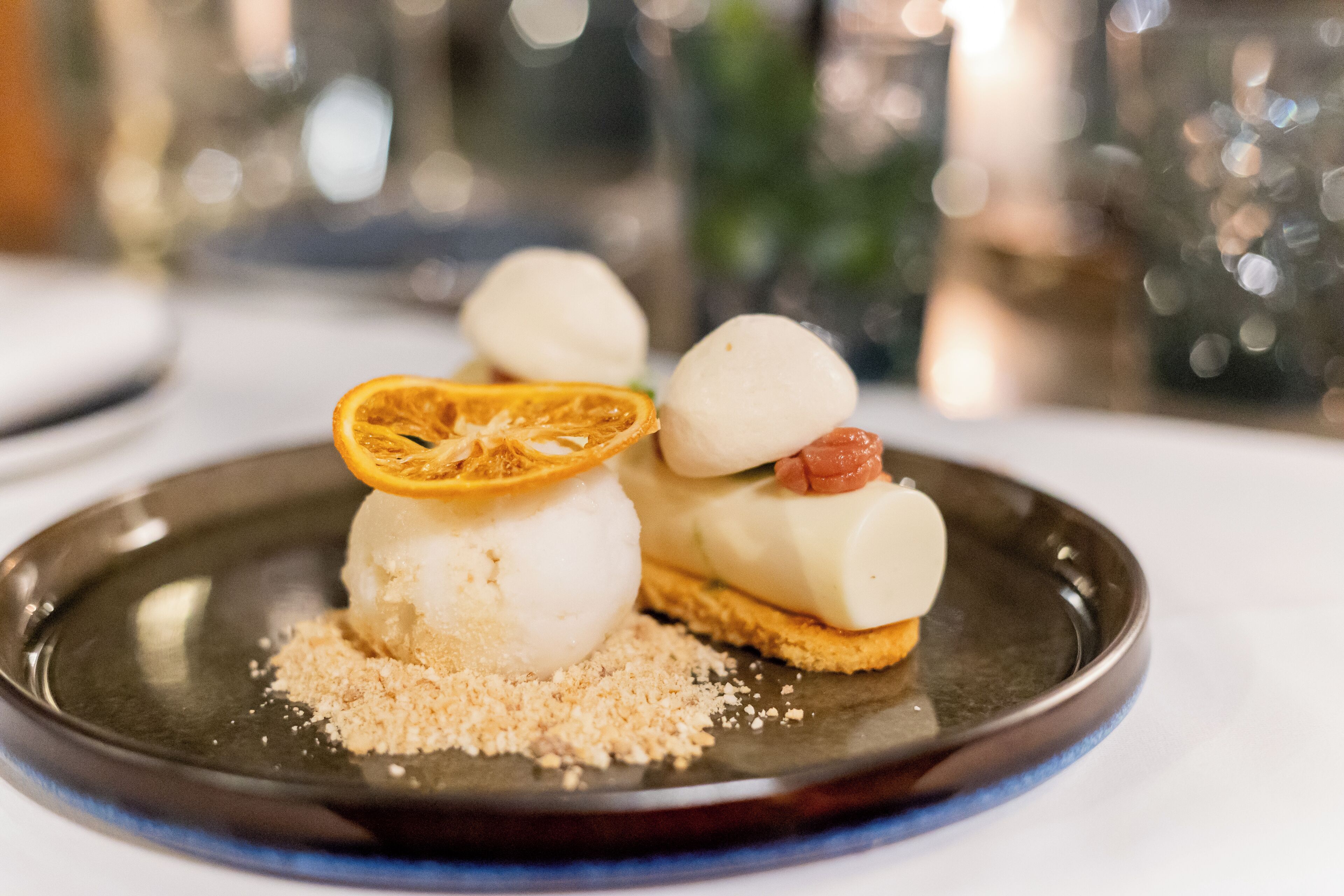 Un dessert présenté dans une assiette, avec une tranche d’orange et un petit morceau de fruit posé sur le dessus.
