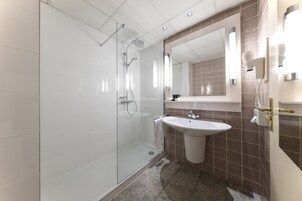 Un baño moderno con cabina de ducha de vidrio, lavamanos pedestal y un espejo grande.