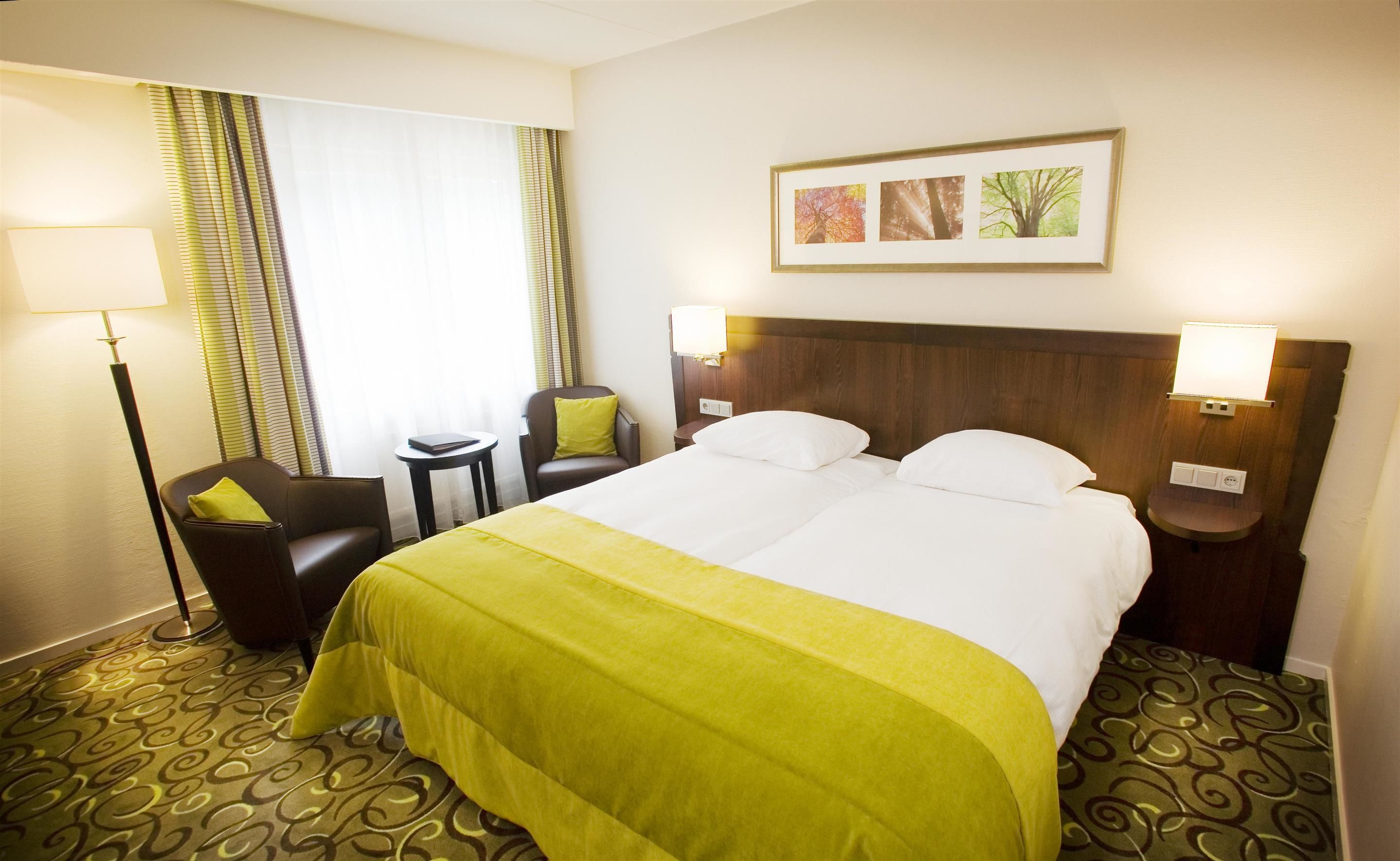 A hotel room with a large bed, two bedside tables, a chair, a lamp, and a framed picture on the wall.