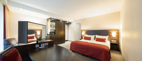 Una habitación de hotel con una cama, un escritorio, una silla, un espejo y una mesita de noche con lámpara.
