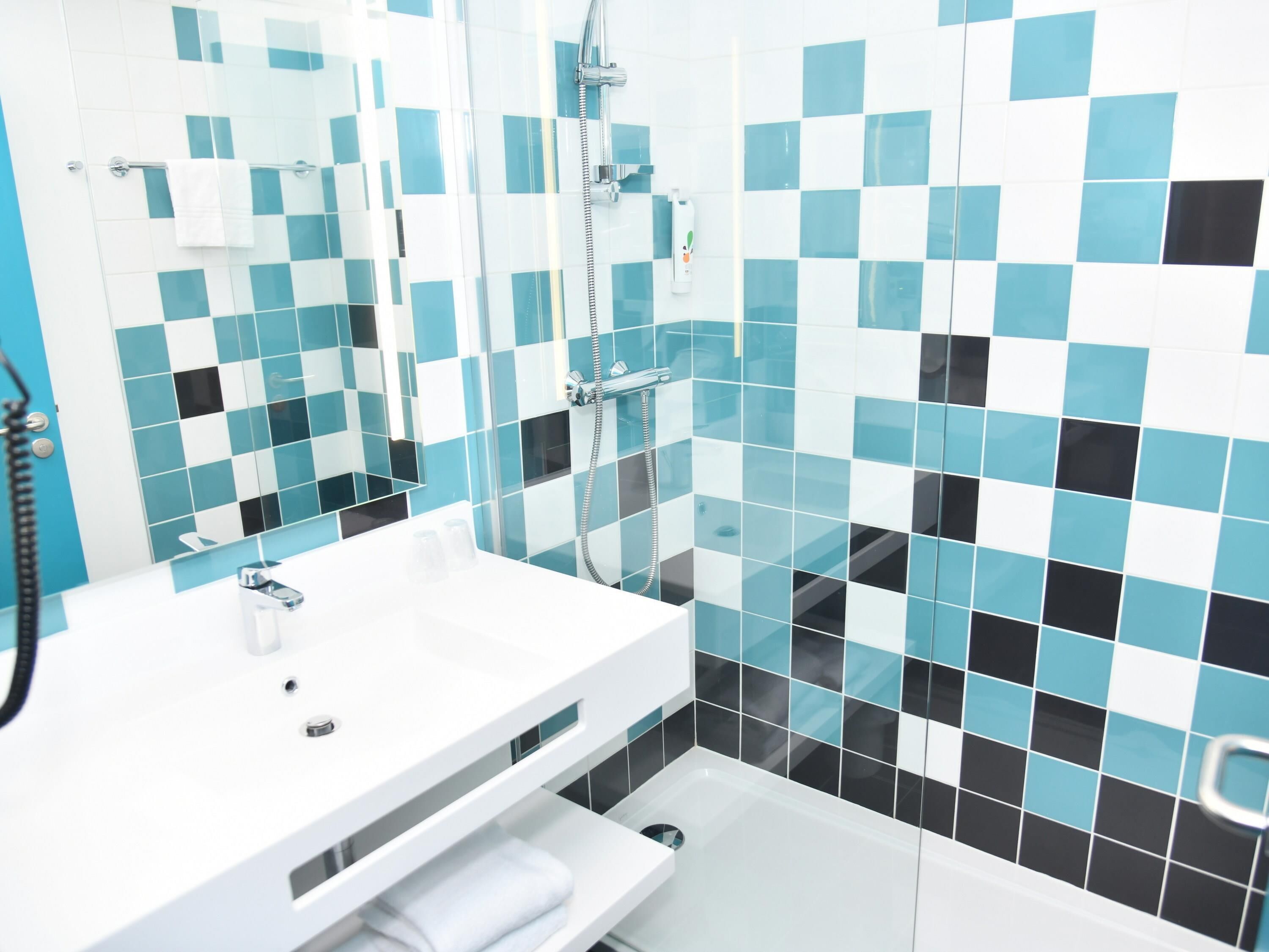 A modern bathroom with a white sink, a glass shower enclosure, and a tiled wall featuring a blue and black pattern.