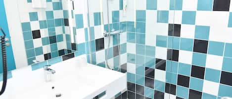 A modern bathroom with a white sink, a glass shower enclosure, and a tiled wall featuring a blue and black pattern.