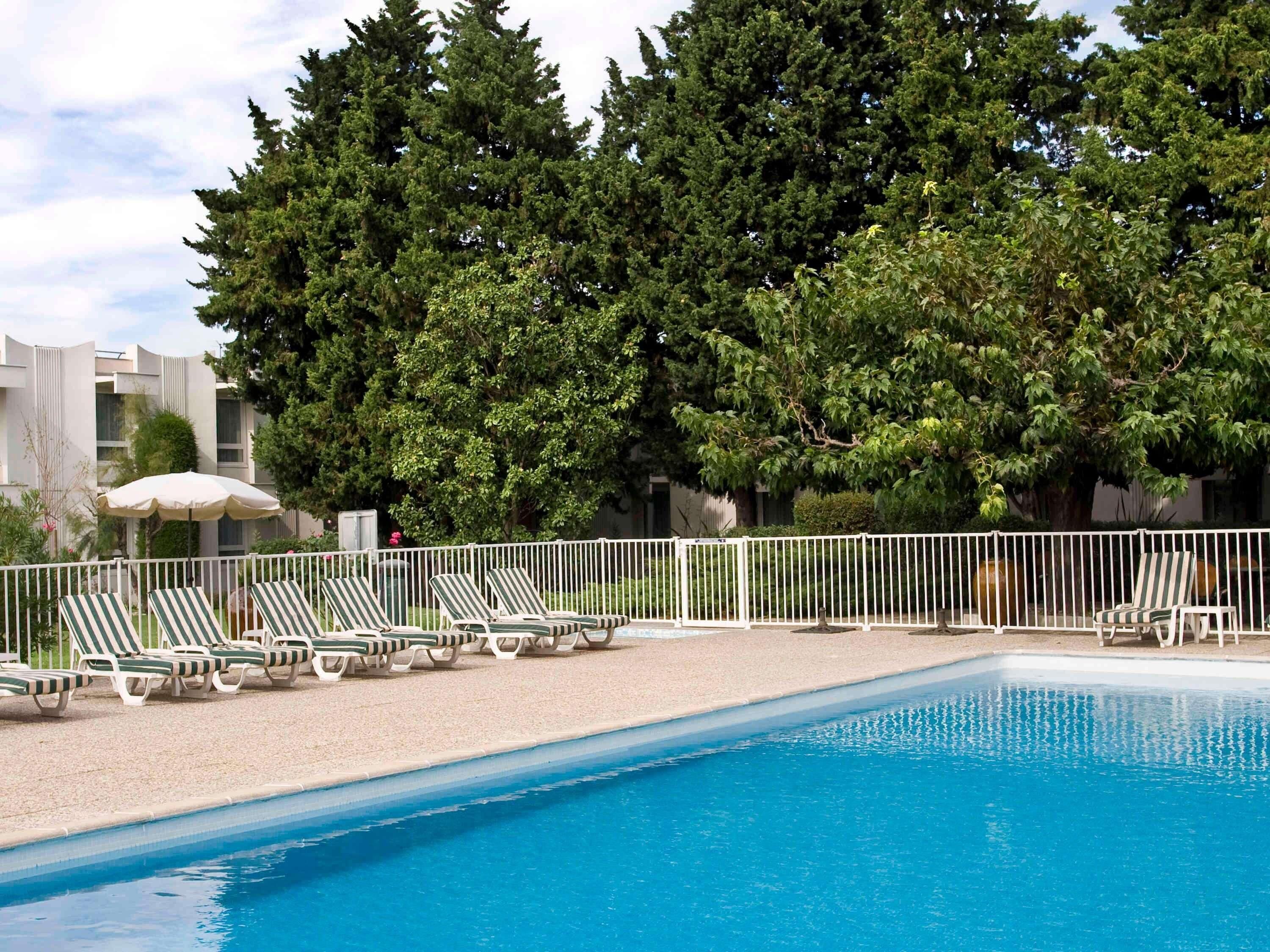 A swimming pool with lounge chairs and a white fence.