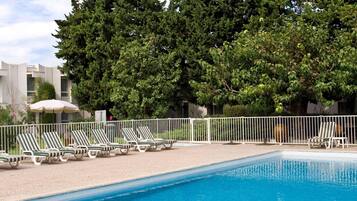A swimming pool with lounge chairs and a white fence.