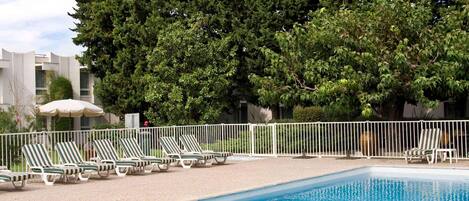 A swimming pool with lounge chairs and a white fence.