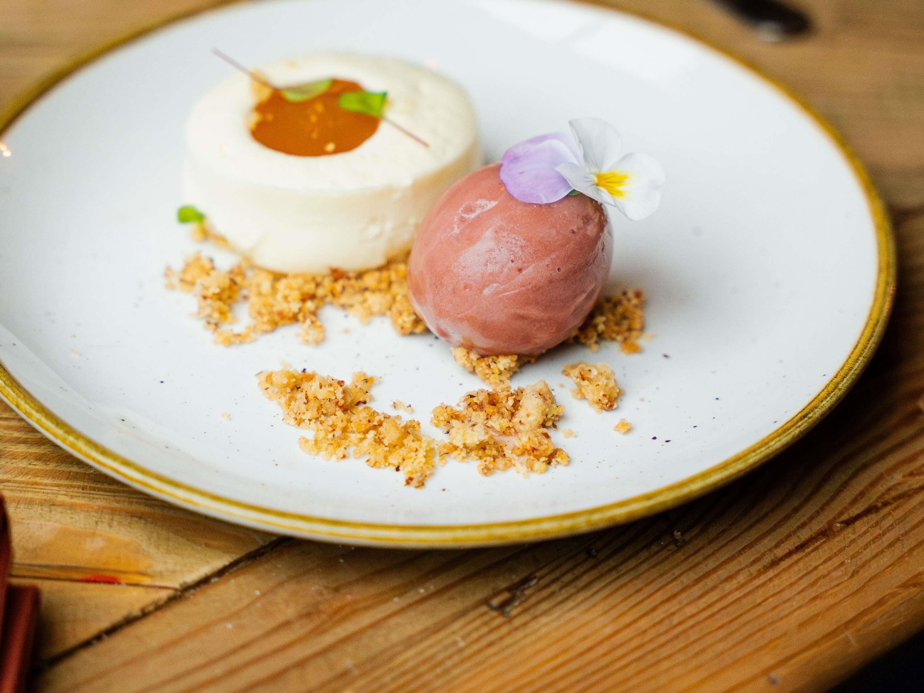A dessert on a plate with crumbs and a flower garnish.