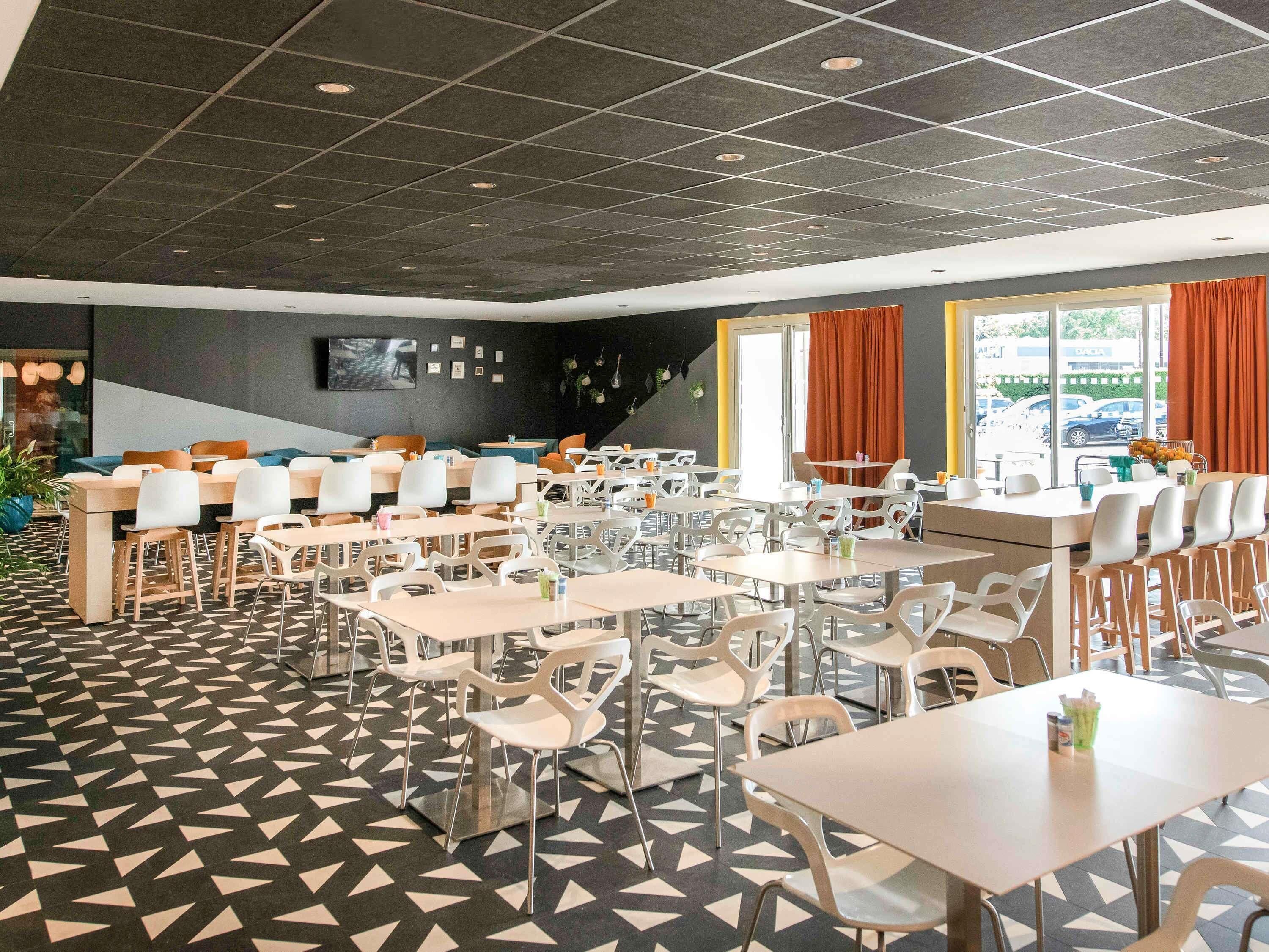 A modern dining area with multiple tables and chairs, a patterned floor, and a large window with curtains.