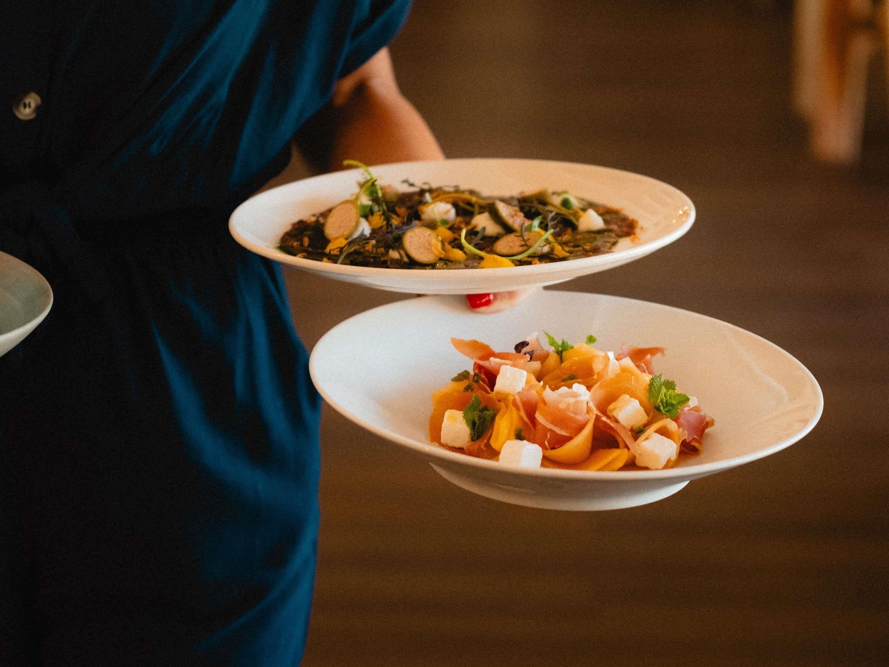 Two white plates with food, held by a person in a dark blue garment.