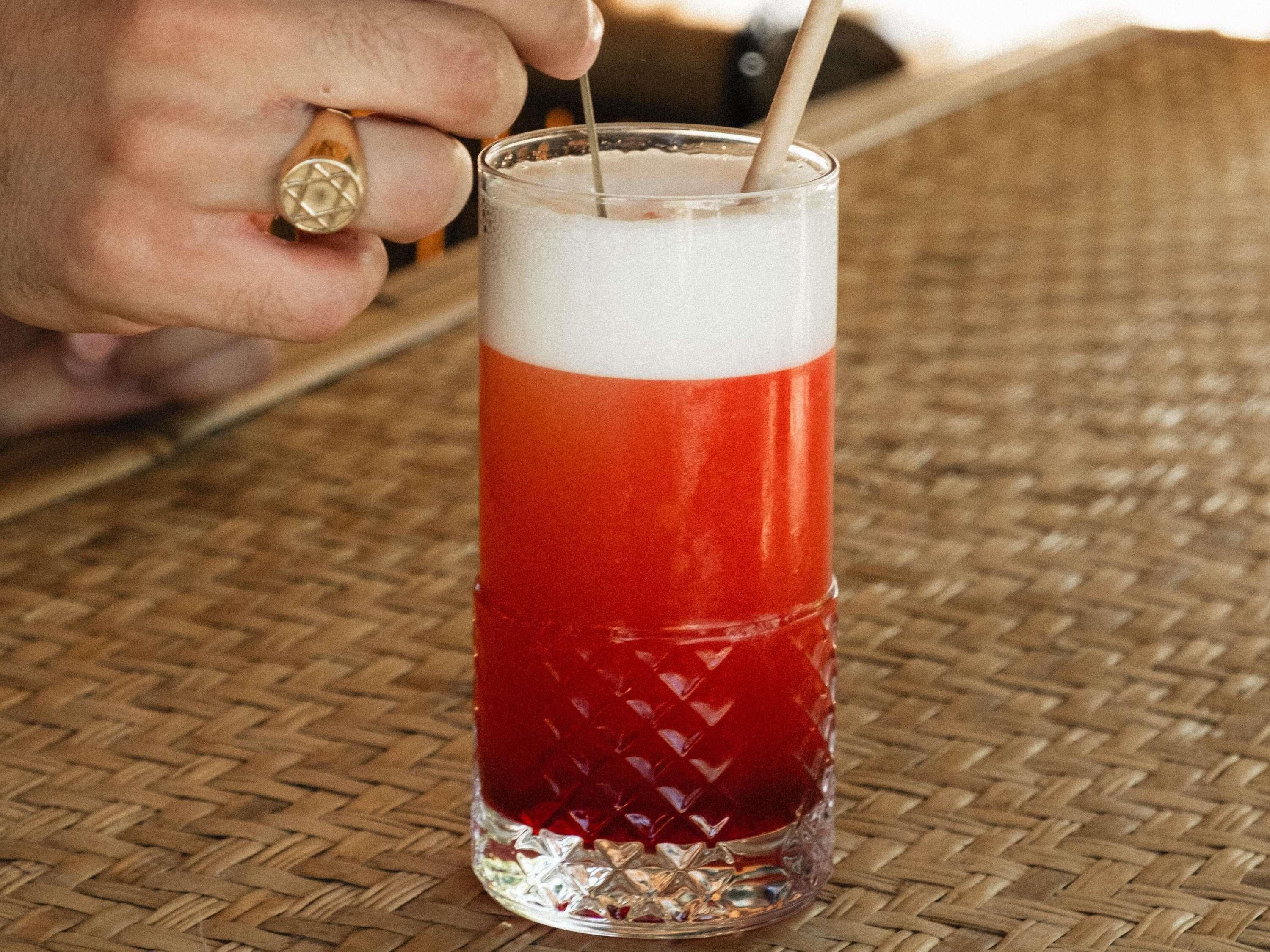 Un bicchiere con una bevanda a strati, una cannuccia e una mano con un anello.