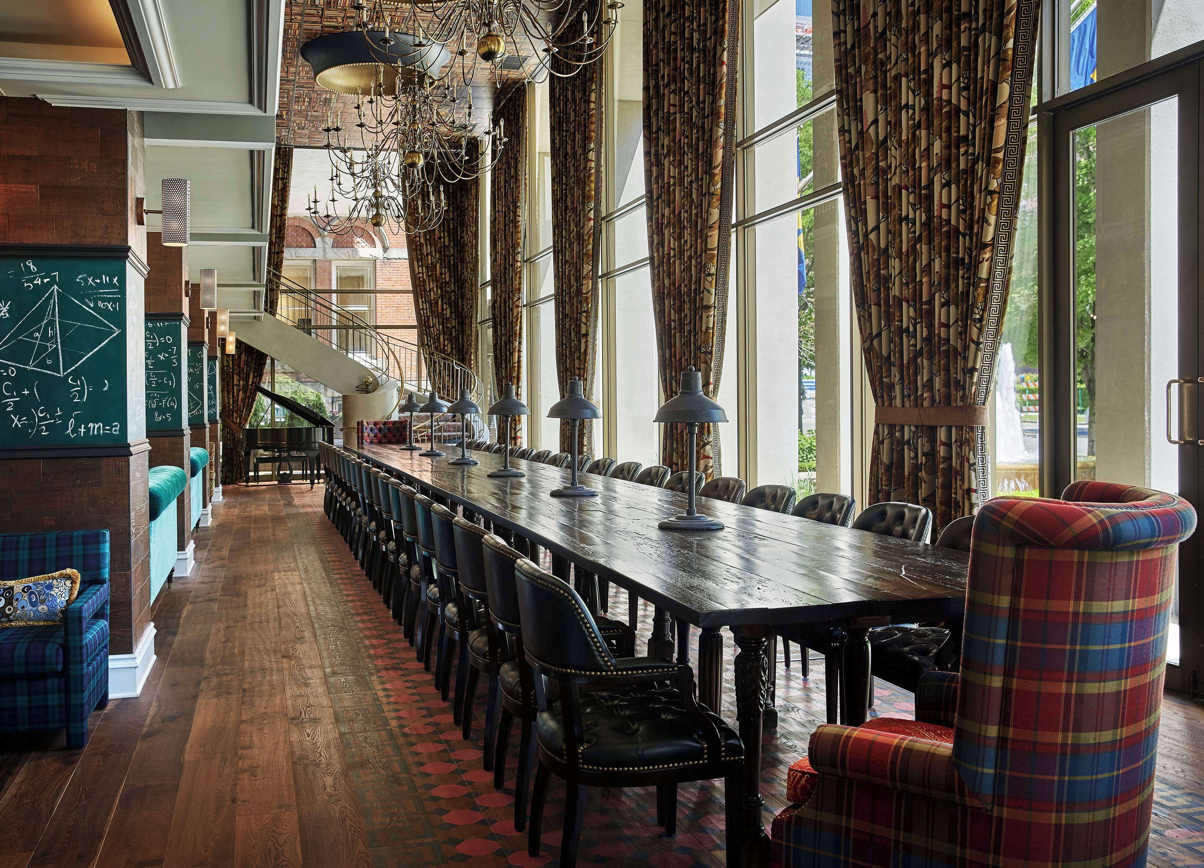 A long dining table with chairs, a chandelier, and curtains.