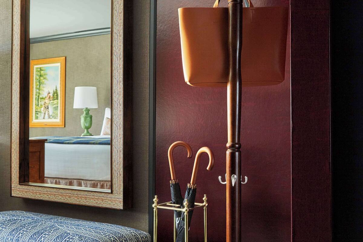 Une pièce avec un grand miroir, un lampadaire, un banc et une petite table sur laquelle se trouvent une lampe et un cadre photo.