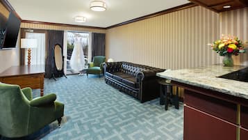 Une chambre d’hôtel avec un canapé, un fauteuil, une table à manger, un miroir et un vase de fleurs.