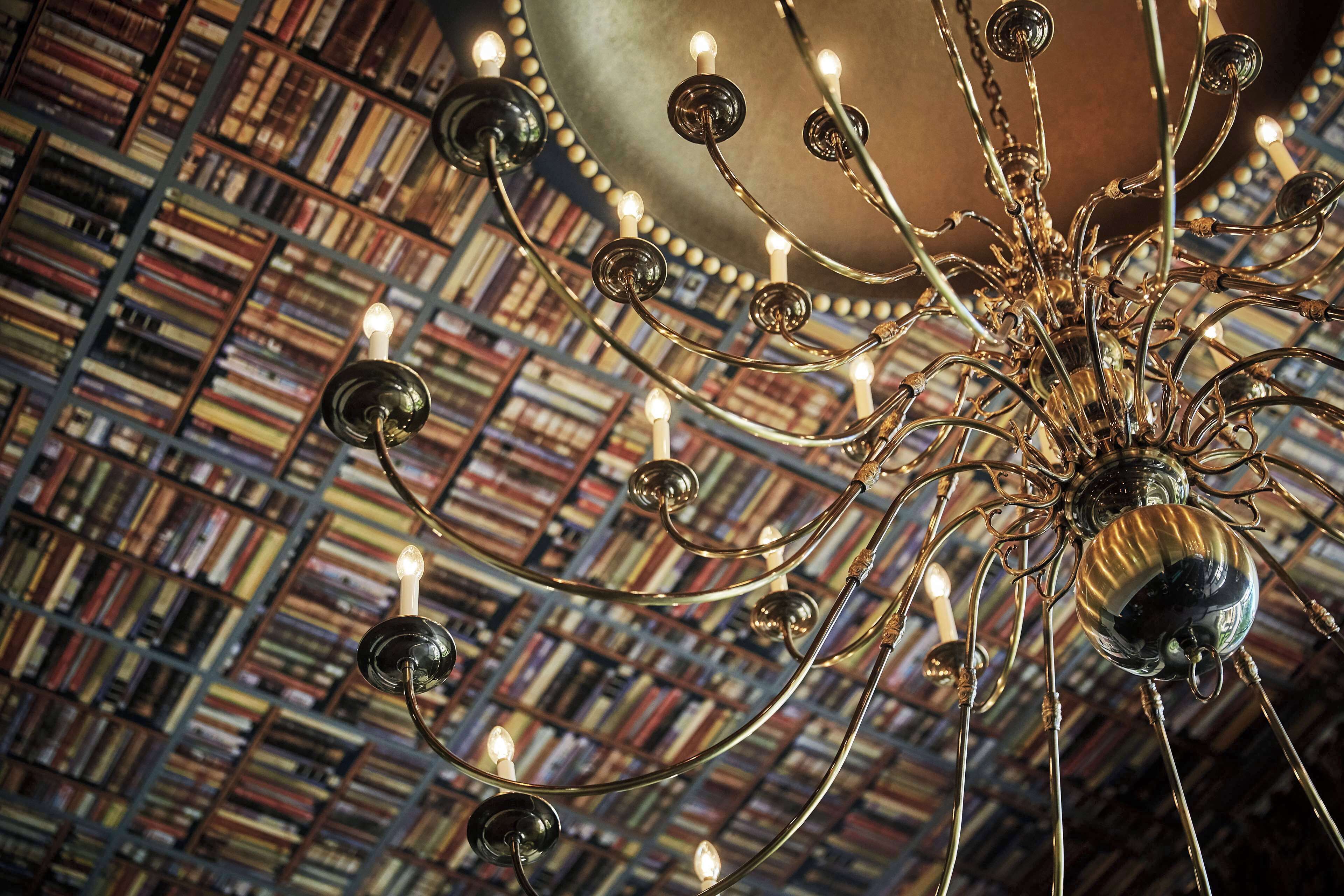 A chandelier with multiple light bulbs in a room with a bookshelf in the background.