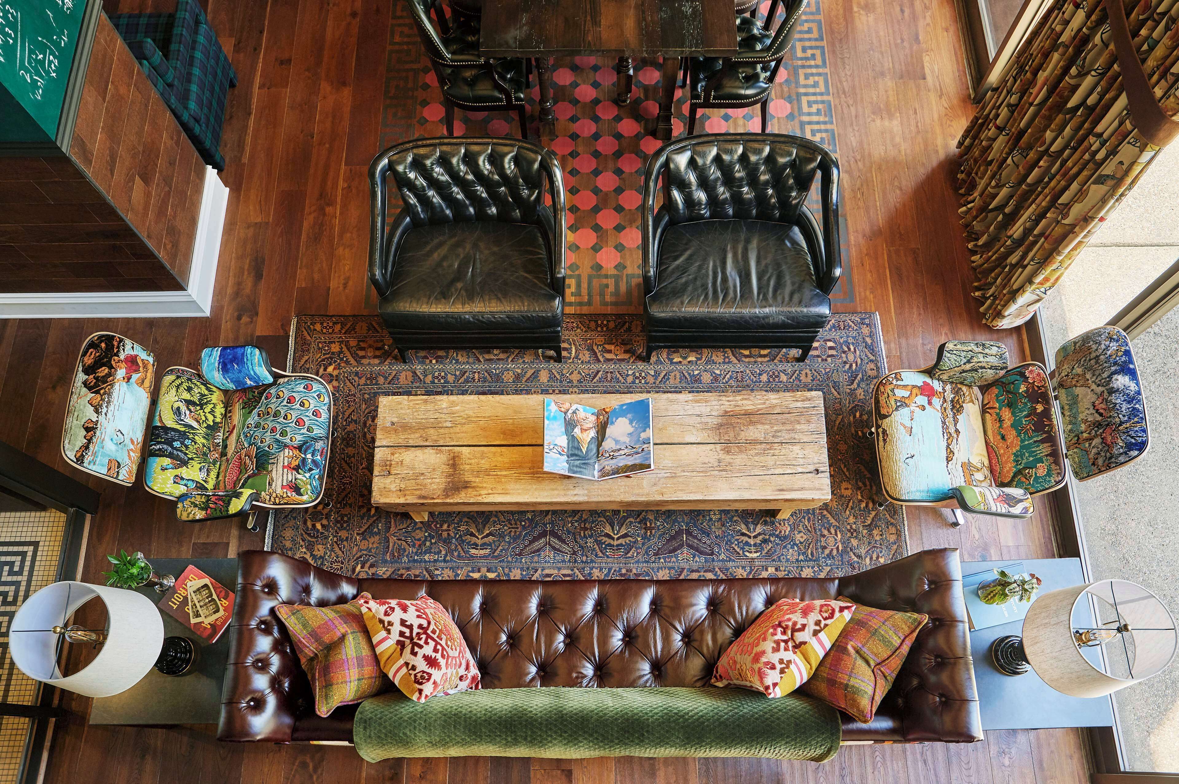 Quarto com sofá de couro marrom, duas poltronas de couro preto, mesa de centro de madeira e malas estampadas.
