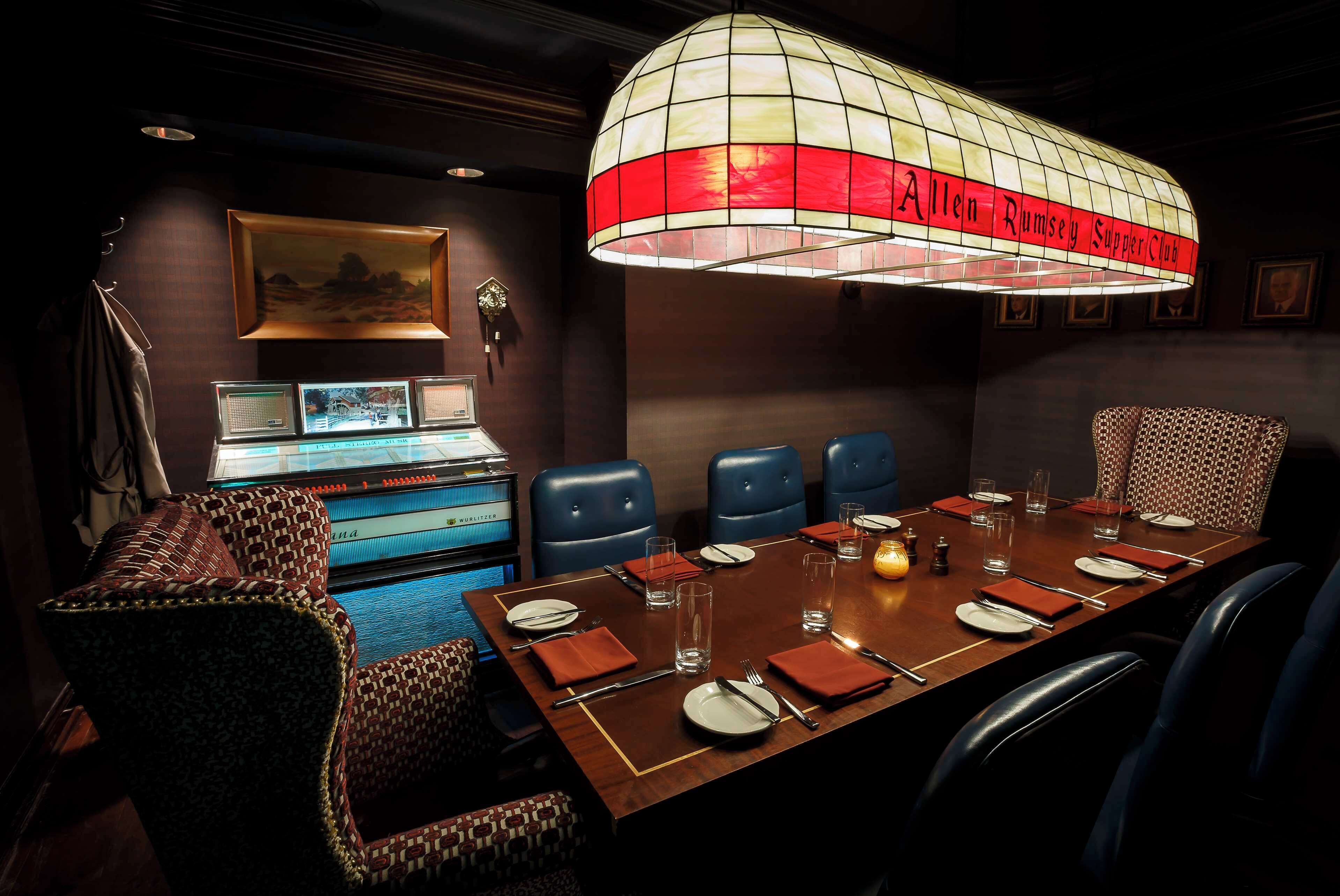 A conference room with a long table set for dining, blue chairs, and a distinctive red and white hanging light fixture.