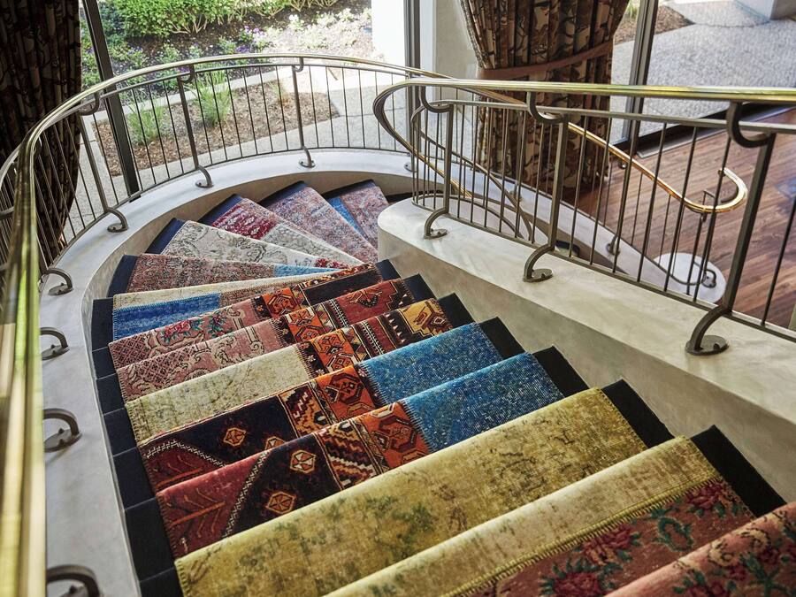 Un escalier agrémenté de différents tapis aux couleurs vives et doté d’une rampe en métal.