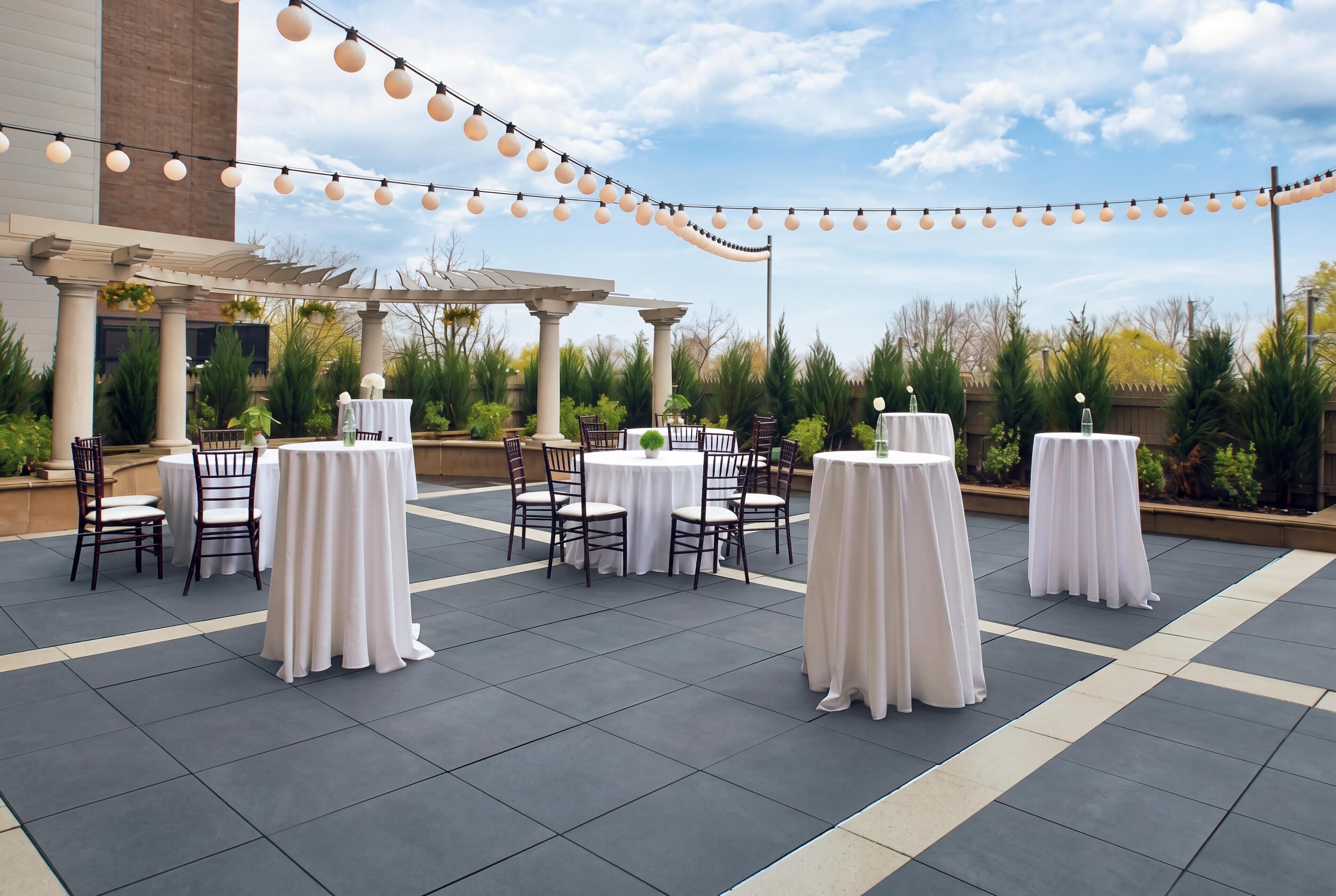An outdoor patio area with round tables and chairs, string lights, and a pergola.