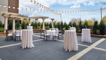 An outdoor patio area with round tables and chairs, string lights, and a pergola.