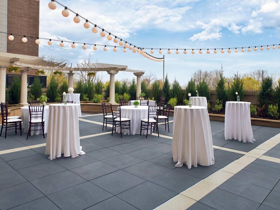 An outdoor patio area with round tables and chairs, string lights, and a pergola.