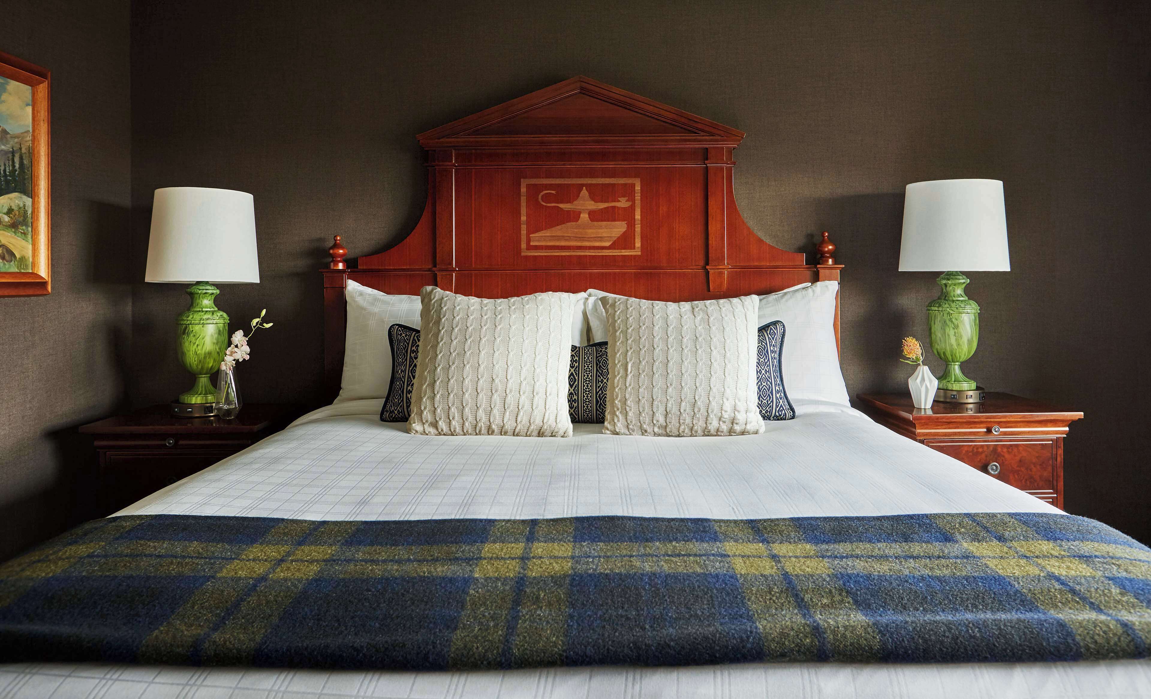 A neatly made bed with a plaid bedspread, two matching pillows, and a wooden headboard with a decorative emblem.