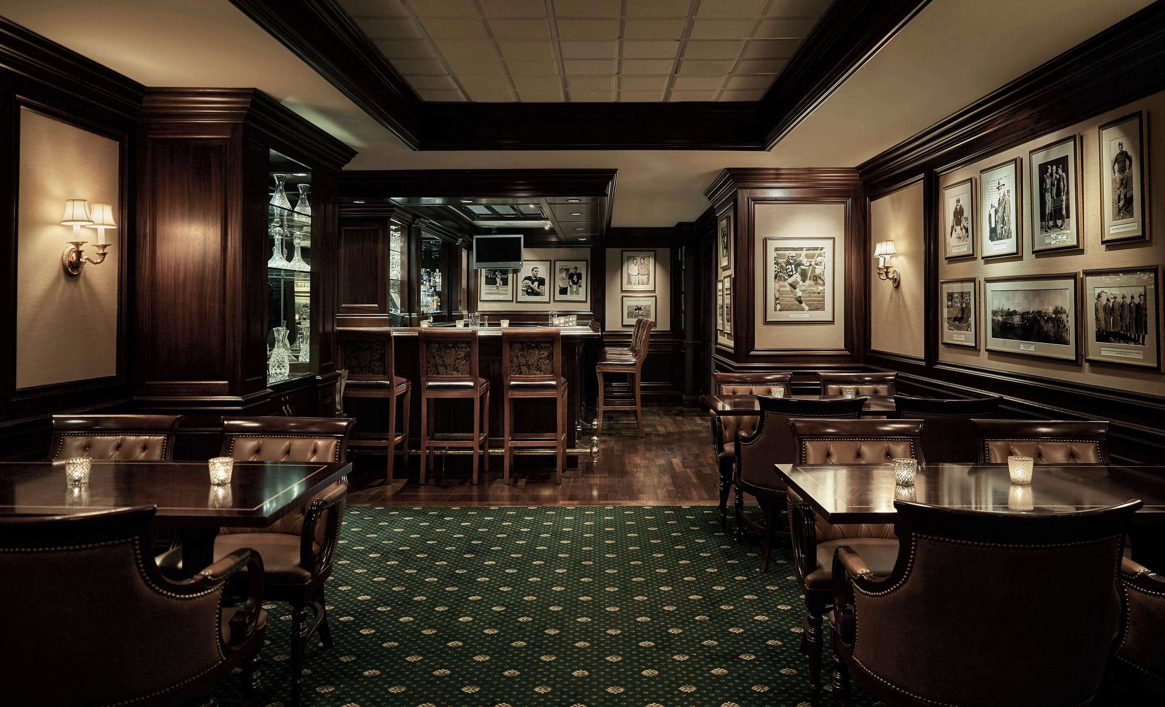 A classic hotel lobby with a bar area, leather seating, and framed historical photographs on the walls.