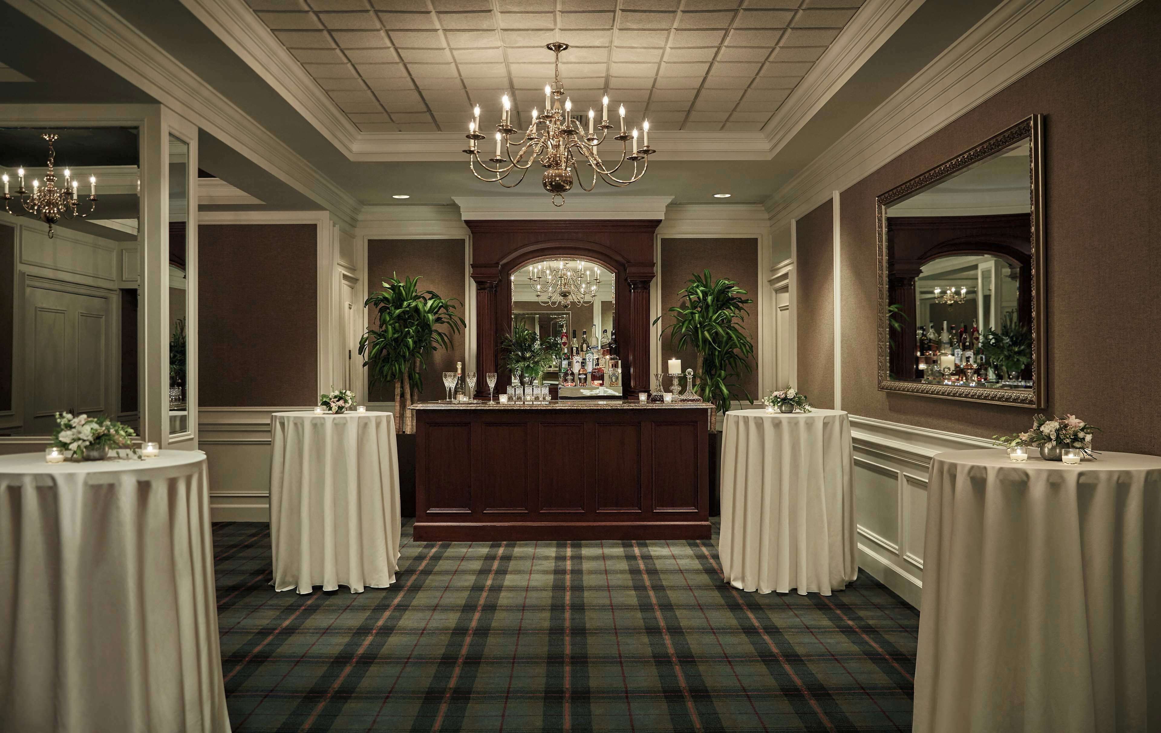 A formal room with a bar area, two round tables with white tablecloths, a chandelier, and a large mirror on the wall.