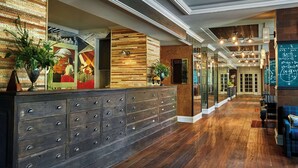 A reception area with a wooden reception desk, multiple drawers, and a large mirror. There are potted plants and a chalkboard with writing on the wall. - Graduate by Hilton Ann Arbor (Ann Arbor)