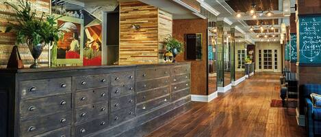 Un espace d’accueil avec un comptoir en bois, de nombreux tiroirs et un grand miroir. On y trouve également des plantes en pot et un tableau noir sur lequel on a écrit au mur.