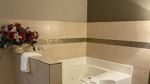 A bathroom with a bathtub, beige tiles, a small flower arrangement, and a towel on the wall. - Super 8 by Wyndham Terrell (Terrell)