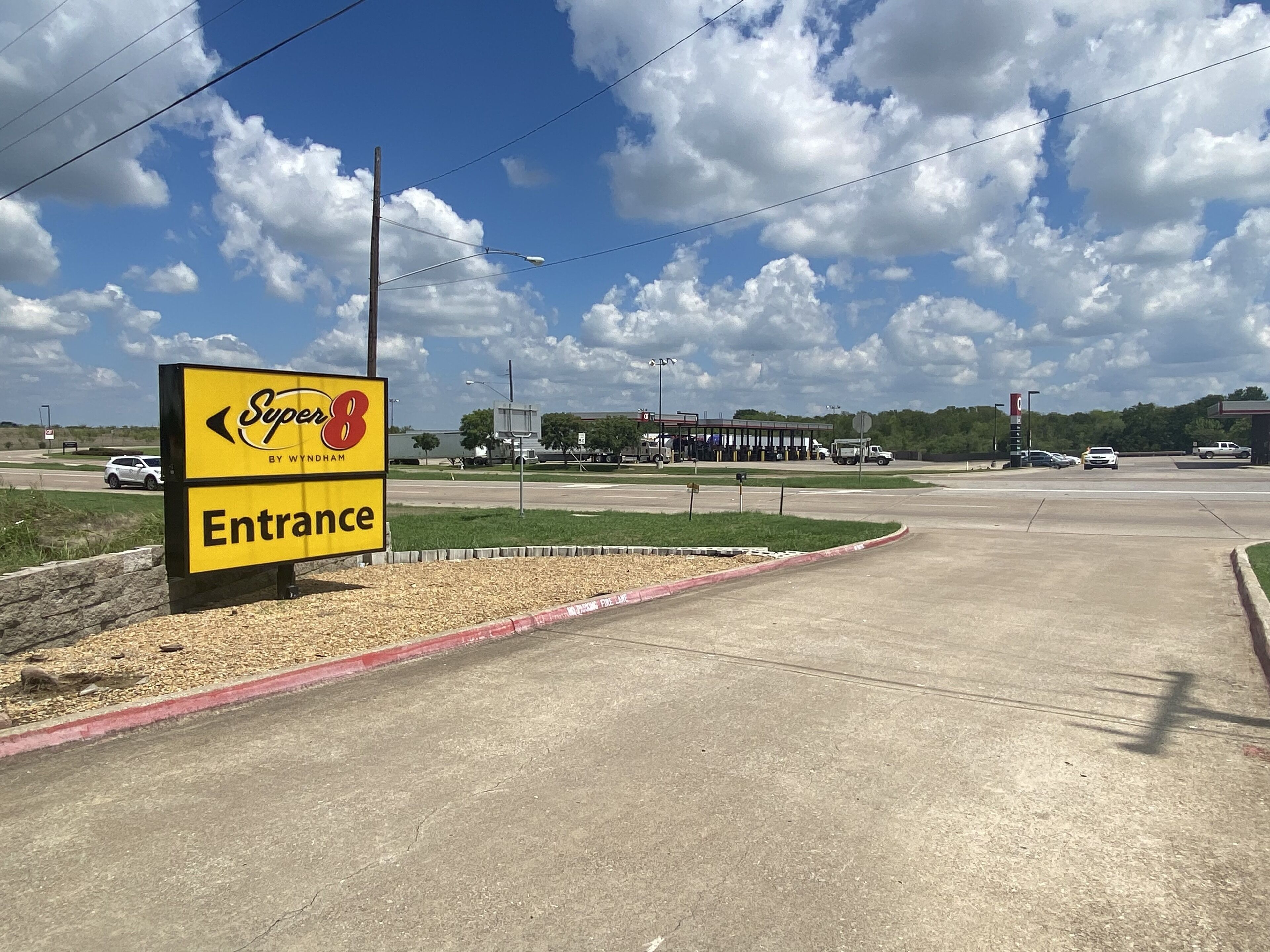 A Super 8 entrance sign with a clear sky and a gas station in the background.
