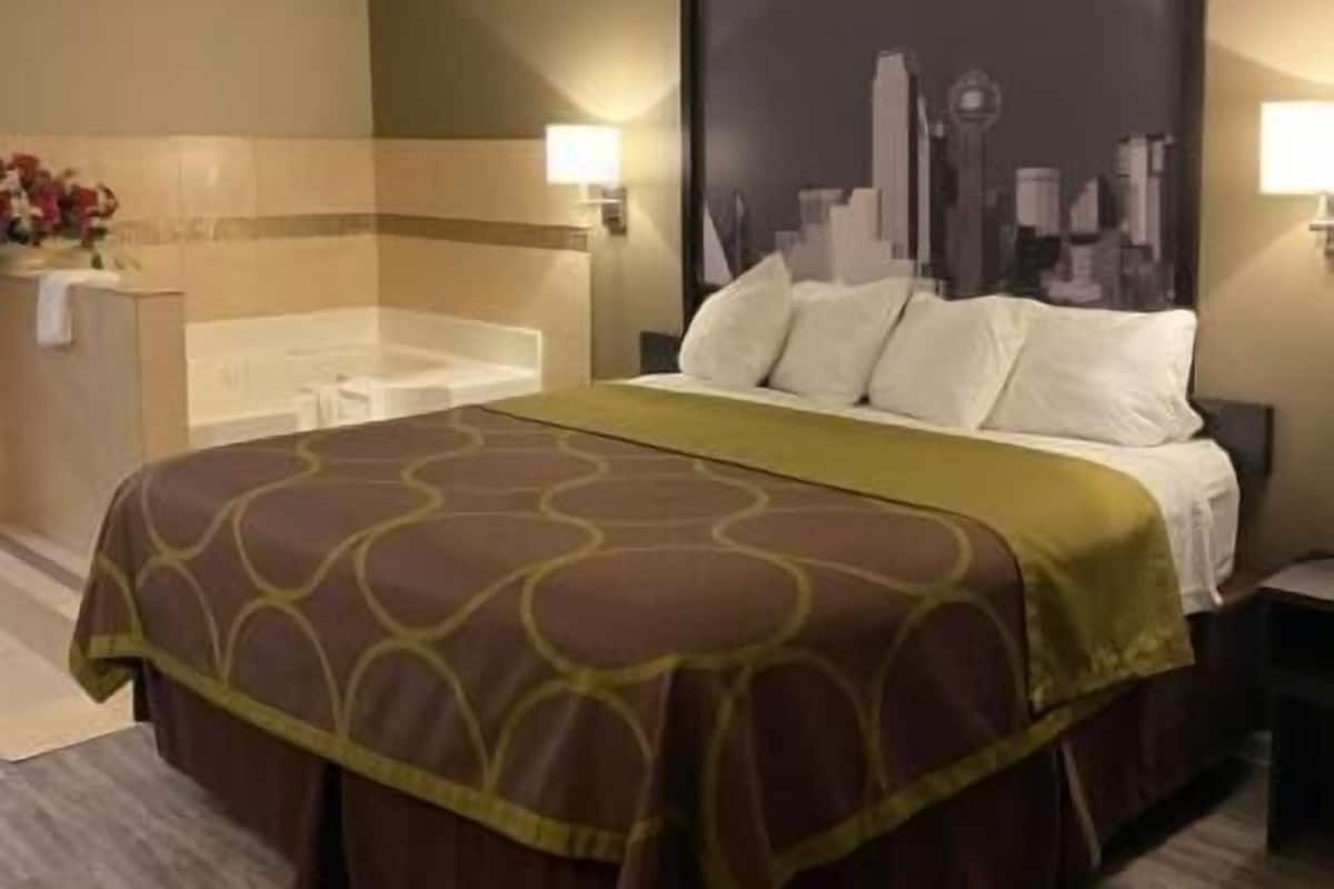 A hotel room with a bed, a nightstand, a wall-mounted lamp, and a cityscape painting.