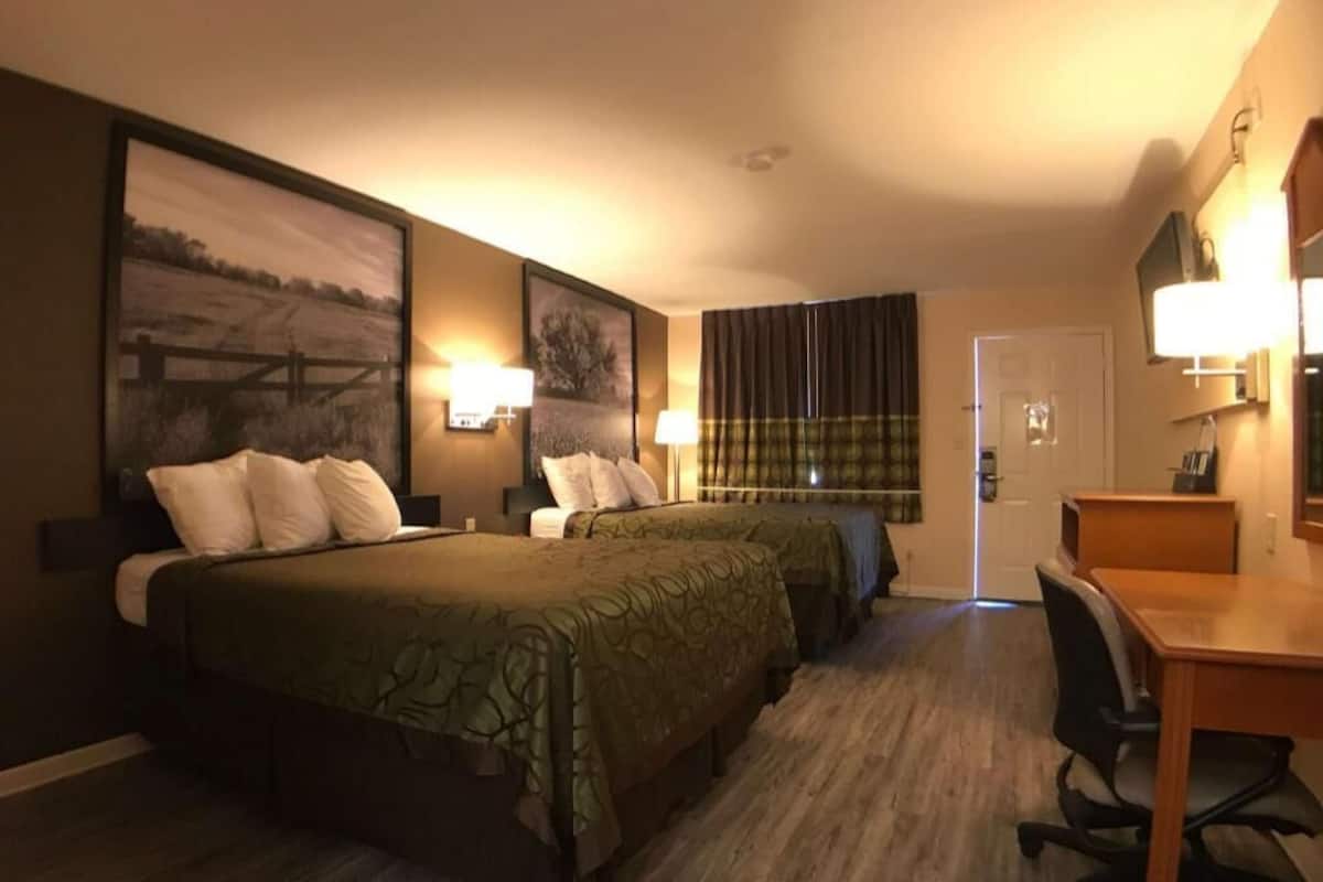 A hotel room with two beds, a desk, a chair, and a door.